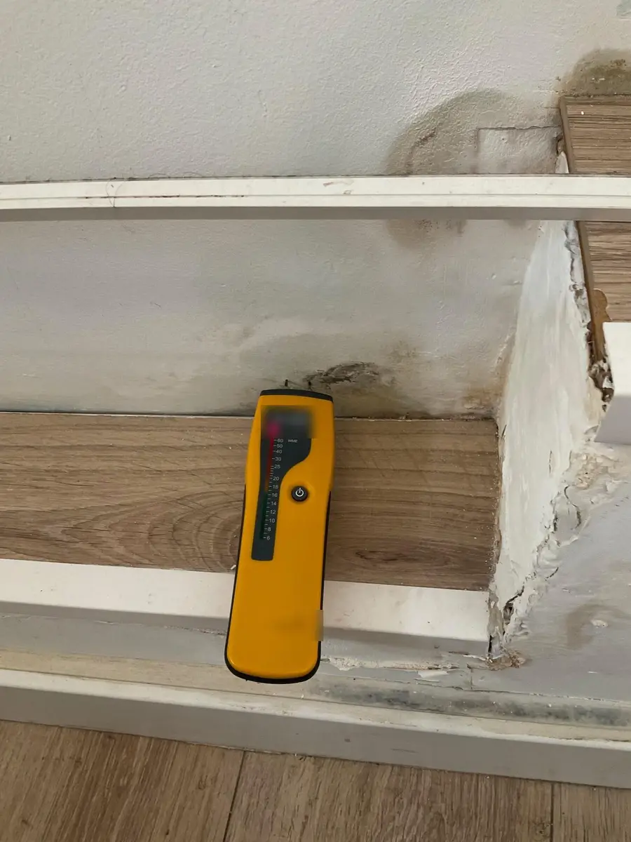 Humidimètre posé contre le bas d'un mur taché d'humidité, au-dessus d'un sol stratifié