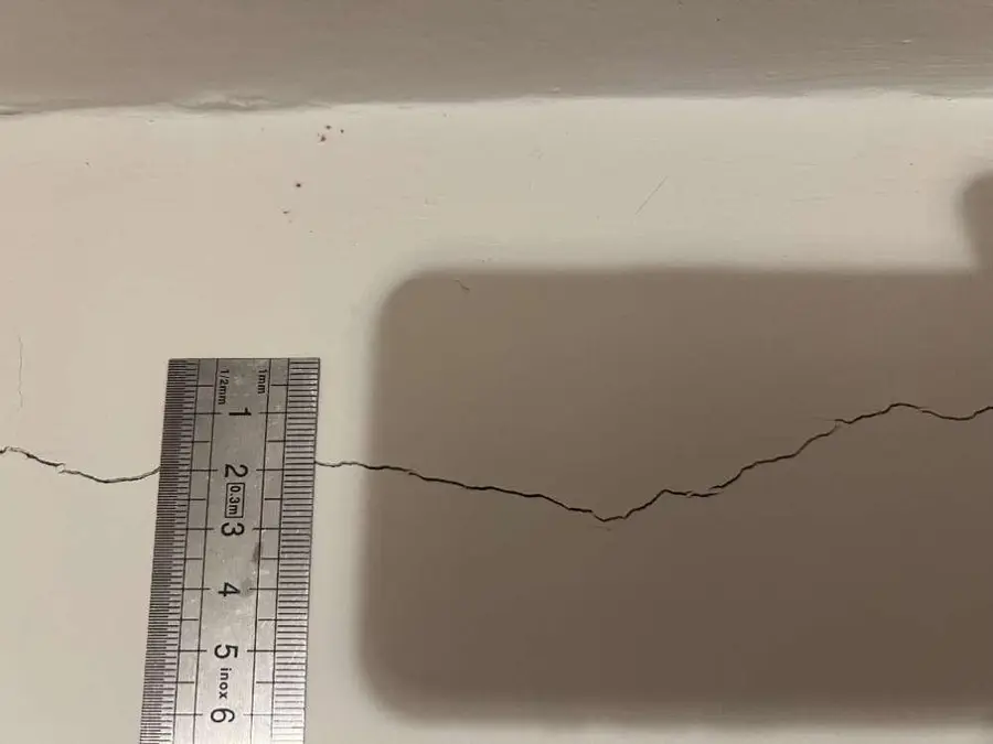 Réglet métallique posé en travers d'une fissure horizontale sur un mur peint en blanc