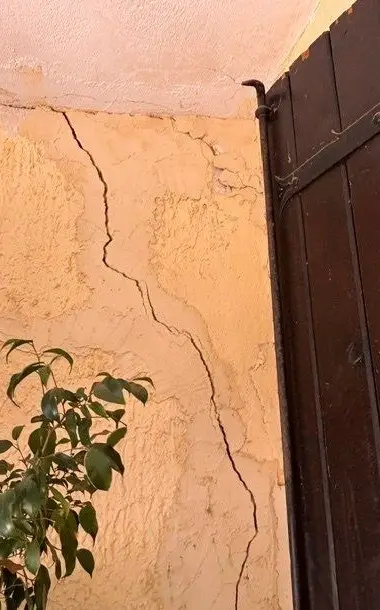 Fissure en escalier dans l'enduit, à l'angle d'une façade, près d'un volet en bois