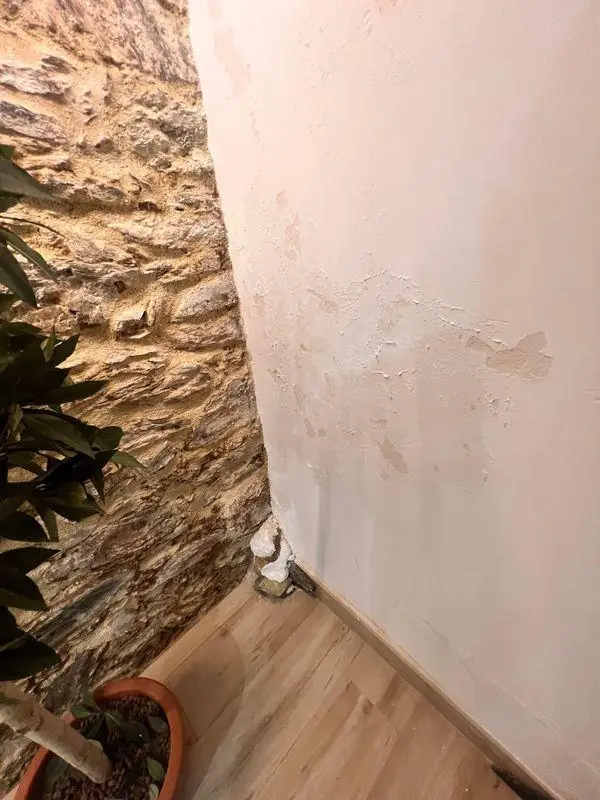 Mur de séjour au plâtre cloqué et écaillé, du pied du mur jusqu'à mi-hauteur, à côté d'un mur en pierre