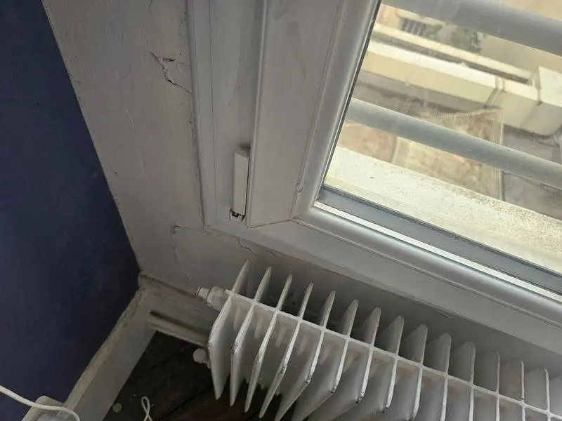 Angle d'une fenêtre à double vitrage sans grille d'aération, plâtre fissuré autour, radiateur dessous